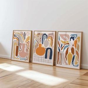 May include: Three abstract art prints with a modern minimalist style. The prints feature a variety of shapes and colors, including orange, blue, yellow, and brown. The prints are framed in natural wood.