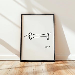 以下が含まれることがあります： 白黒の線画で描かれたダックスフント。右下に「ピカソ」の署名があります。黒い額縁に収められ、白い壁に掛けられています。