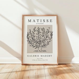 Pode incluir: Uma impressão emoldurada com um desenho minimalista de uma árvore em preto sobre um fundo bege. O texto "MATISSE LE PLATANE" está no topo da impressão, e "GALERIE MAEGHt Paris 1924 12 Rue de Téhéran, Paris VIII" está na parte inferior.