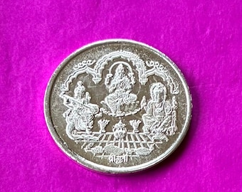 May include: A silver coin featuring three seated figures within an arched frame. Intricate details depict the figures and surrounding design. The coin is set against a vibrant magenta background.