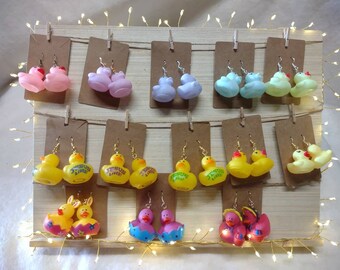 May include: A display of colorful rubber ducky earrings. The earrings are arranged on a wooden board with clips. Some of the ducks have the words "Jesus Lives" printed on them.
