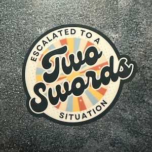 May include: A round sticker with the text "ESCALATED TO A TWO SWORDS SITUATION" in a retro font. The sticker has a cream-colored background with a sunburst design in orange, yellow, and blue. The sticker is on a gray surface.