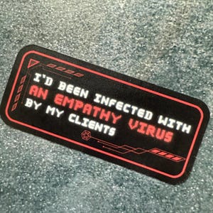 May include: A rectangular black sticker with a red border and text that reads "I'D BEEN INFECTED WITH AN EMPATHY VIRUS BY MY CLIENTS" in white and red. The sticker has a tech-inspired design.