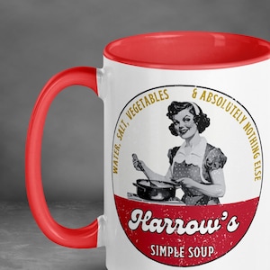 May include: White ceramic mug with a red interior and handle. The mug features a vintage-style illustration of a woman cooking, with text that reads "Water, Salt, Vegetables & Absolutely Nothing Else" and "Harrow's Simple Soup."
