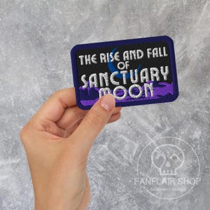May include: A rectangular patch with the text "THE RISE AND FALL OF SANCTUARY MOON" in white, blue, and purple. The patch has a dark blue border and is held by a hand. The Fanflair Shop logo is in the bottom right corner.