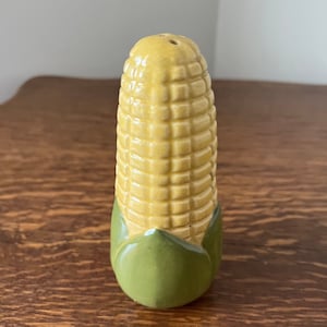 May include: A ceramic corn on the cob salt and pepper shaker. The corn is yellow with green husks.