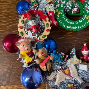 May include: A festive Christmas wreath with various ornaments, including a pig in a yellow scarf, a clown, a rocking horse, and a nutcracker. The wreath includes a green circular sign that reads "Tis The Season To Be Jolly".