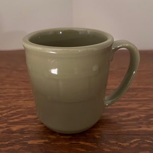 May include: A green ceramic mug with a textured design. The mug has a rounded shape and a handle.