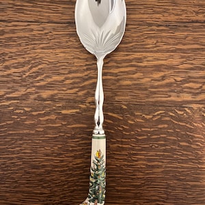 May include: A silver spoon with a white ceramic handle featuring a green Christmas tree design.