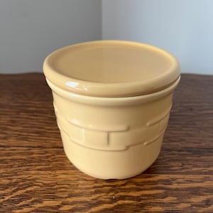 Peut inclure: Un pot en céramique jaune avec un couvercle, présentant un motif de panier tissé. Le pot est sur une surface en bois.