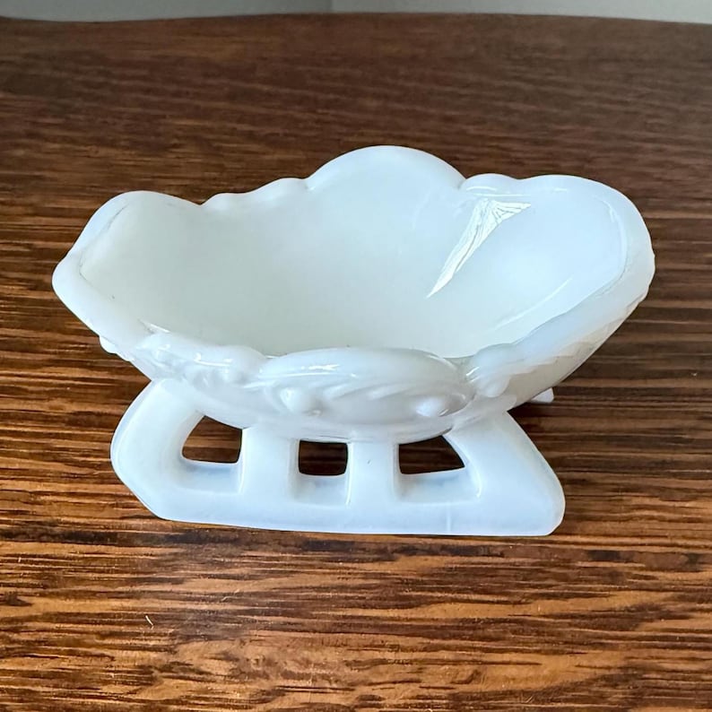 Small white milk glass sleigh-shaped dish with curved edges and raised decorative detailing.