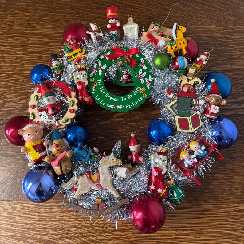 Handmade 12 inch vintage Christmas ornament wreath featuring assorted small figurines, glass ornaments, and silver tinsel garland arranged in a circular wreath form.