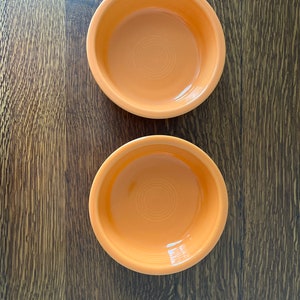 May include: Two orange ceramic bowls on a wooden surface. The bowls are empty and have a smooth, glossy finish.