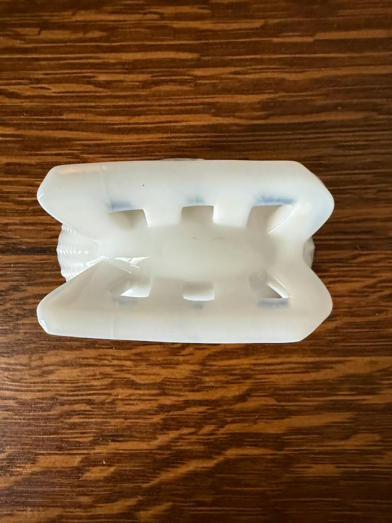 May include: A white, rectangular object with a series of rectangular cutouts. The object has a curved top and bottom, and appears to be made of a translucent material. The object is resting on a wooden surface.