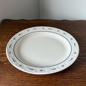 May include: A white ceramic plate with a blue and white patterned border. The pattern features a repeating design of small flowers and wavy lines.