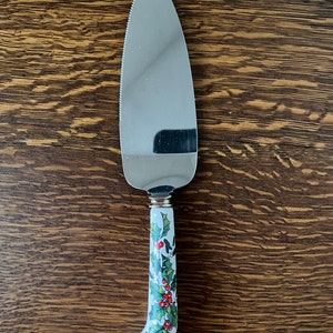 May include: A silver cake server with a white handle decorated with a green holly and red berry design.