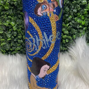 May include: A blue and gold tumbler featuring a cartoon image of a person wearing glasses and a moustache. The tumbler is covered in rhinestones and has the word "remarkable" written on it.