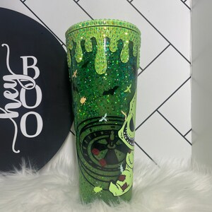 Peut inclure: Un gobelet vert &agrave; paillettes avec un motif de goutte de slime vert. Le gobelet pr&eacute;sente une illustration en noir et blanc d'un personnage de L'&Eacute;trange No&euml;l de monsieur Jack tenant une roulette. Le gobelet a une base et un couvercle en paillettes vertes.