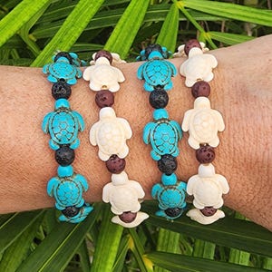 May include: Four stretch bracelets featuring alternating sea turtle charms and small round beads. Two bracelets consist of turquoise-colored turtle charms with black porous beads, while the other two feature off-white turtle charms with dark brown beads.
