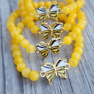May include: Three yellow beaded bracelets with gold butterfly charms. The butterflies have black and white wings.