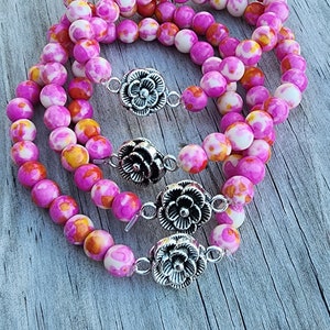 May include: Three pink and orange patterned beaded bracelets with silver flower clasps.