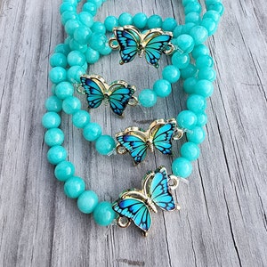 May include: Three turquoise beaded bracelets with gold butterfly charms. The butterflies have blue and black wings.
