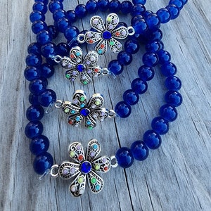 May include: Four blue beaded bracelets with silver flower charms. Each charm has a blue rhinestone center and colorful rhinestones around the edges.