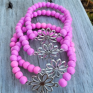 May include: Three pink beaded bracelets with silver daisy charms. The bracelets are stacked on top of each other.