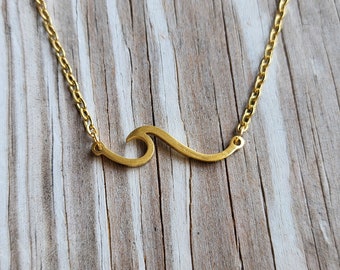 May include: A gold chain necklace with a wave-shaped pendant. The pendant is made of metal and has a smooth, polished finish.