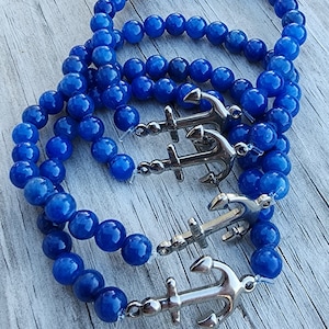 May include: Three blue beaded bracelets with silver anchor charms. The bracelets are made of round beads and are stacked on top of each other.
