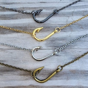 May include: Four necklaces featuring a fish hook pendant attached to a matching metal chain. The set includes one black, one gold-tone, one silver-tone, and one antique bronze-tone necklace, each showcasing a simple hook design.