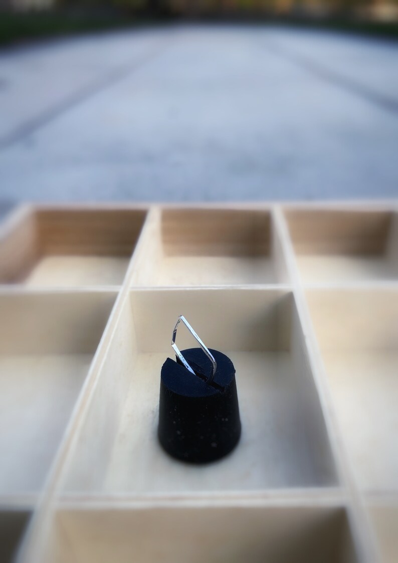 May include: A black rubber stopper with a silver metal handle, set inside a light-colored wooden organizer with multiple compartments. The stopper is the focal point, with the handle angled upwards.