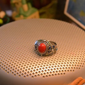 May include: A silver ring featuring a red oval gemstone surrounded by blue and green enamel flowers.