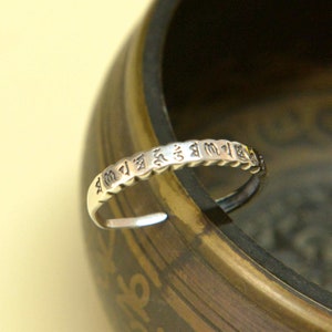 Op de afbeelding: Een zilveren ring met een band van kleine, verhoogde cirkels. De ring is beschreven met een reeks karakters in een vreemde taal.