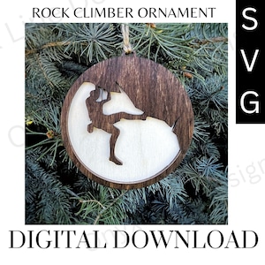 May include: A wooden Christmas ornament featuring a silhouette of a rock climber on a rock face. The ornament is brown with a white center and is hanging from a pine tree branch.