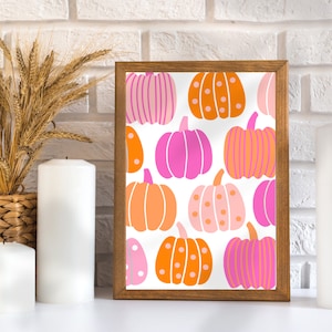 May include: A framed print with a white background and a repeating pattern of pink, orange, and peach pumpkins. The pumpkins have different designs, including polka dots, stripes, and solid colors.