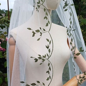 May include: White tulle wedding veil with a green leafy vine embroidery pattern.