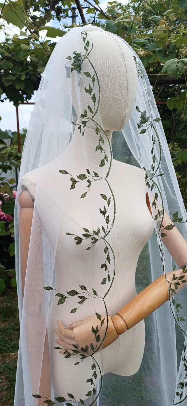 May include: White tulle wedding veil with a green leafy vine embroidery pattern.