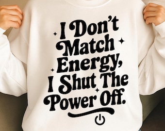 May include: White sweatshirt with the text "I Don't Match Energy, I Shut The Power Off" in a bold, black font. The design includes star accents and a power button symbol. A casual, comfortable top.