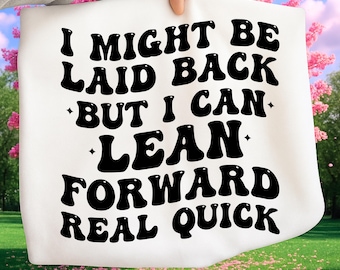 Puede incluir: Una bolsa de mano blanca con el texto "I MIGHT BE LAID BACK BUT I CAN LEAN FORWARD REAL QUICK" en letras negras en negrita. La bolsa se sostiene contra un fondo de flores rosas y hierba verde.