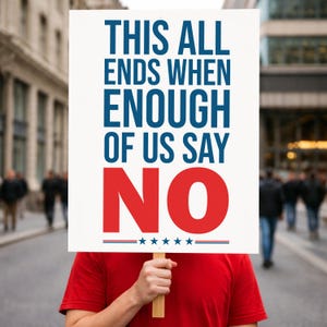 May include: A person holding a white sign with the text "THIS ALL ENDS WHEN ENOUGH OF US SAY NO" in blue and red. The sign is held on a wooden stick. The person is wearing a red shirt, and people are walking in the background.