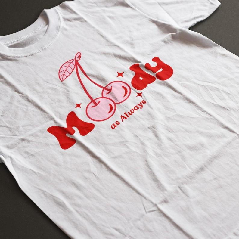 May include: White t-shirt with a red graphic of two cherries and the text "Moody as Always".
