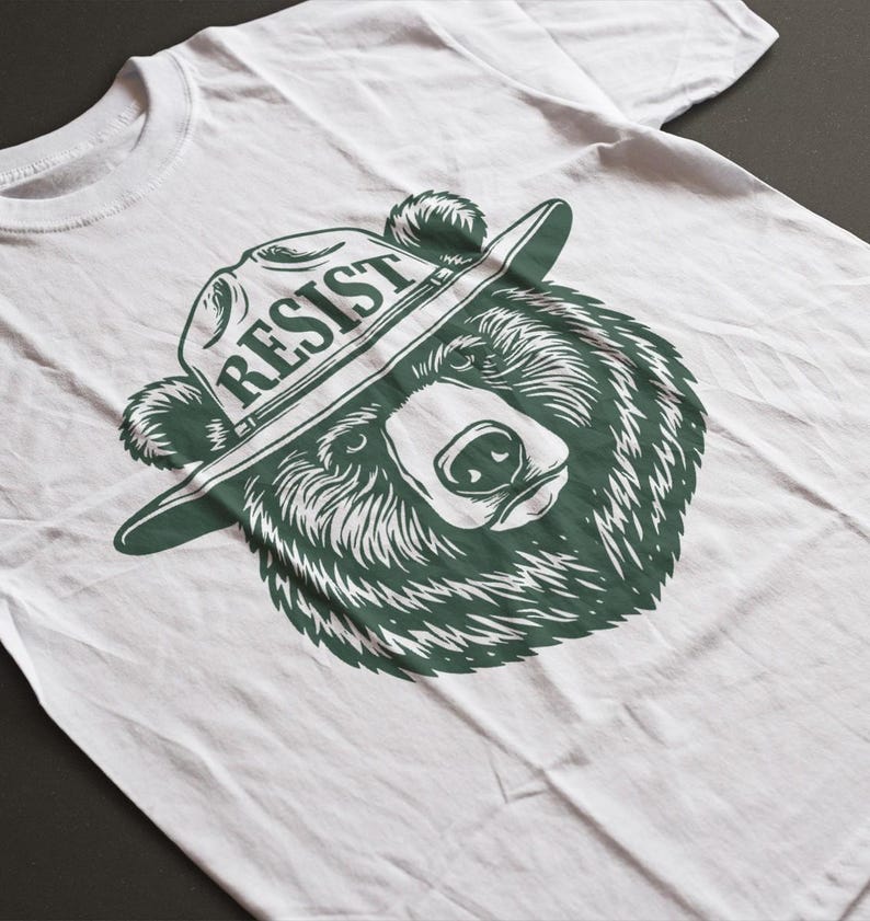 May include: White t-shirt with a green graphic of a bear wearing a ranger hat with the word "RESIST" on it.