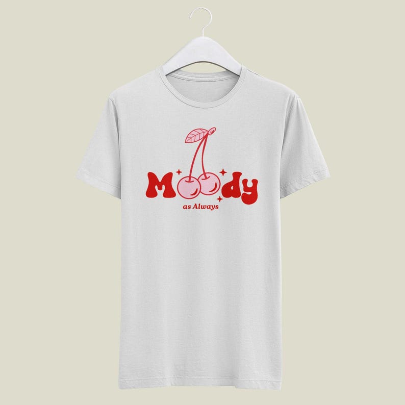 May include: White t-shirt with a red graphic of two cherries and the text "Moody as Always".