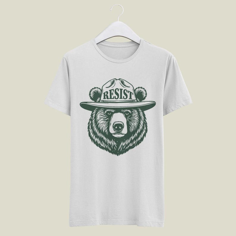 May include: White t-shirt with a black and white illustration of a bear wearing a ranger hat with the word "RESIST" on it.