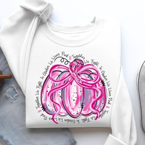 May include: White sweatshirt featuring a pink pumpkin design with a ribbon and the text "Together We Fight, In October We Wear Pink". The pumpkin has pink and gray accents, and the text is in a circular arrangement.