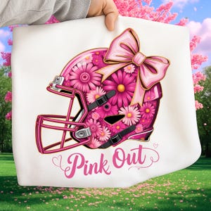 May include: White square fabric with a pink football helmet design. The helmet is decorated with pink flowers and a pink bow. The words "Pink Out" are written in pink script below the helmet.