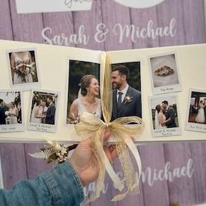 May include: A wedding photo album with multiple photos, including images of the couple, rings, and their first dance. The album is tied with a beige ribbon. The names "Sarah & Michael" are written on the background.