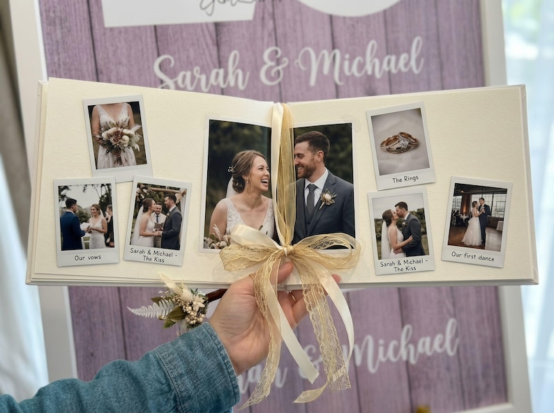 May include: A wedding photo album with multiple photos, including images of the couple, rings, and their first dance. The album is tied with a beige ribbon. The names "Sarah & Michael" are written on the background.