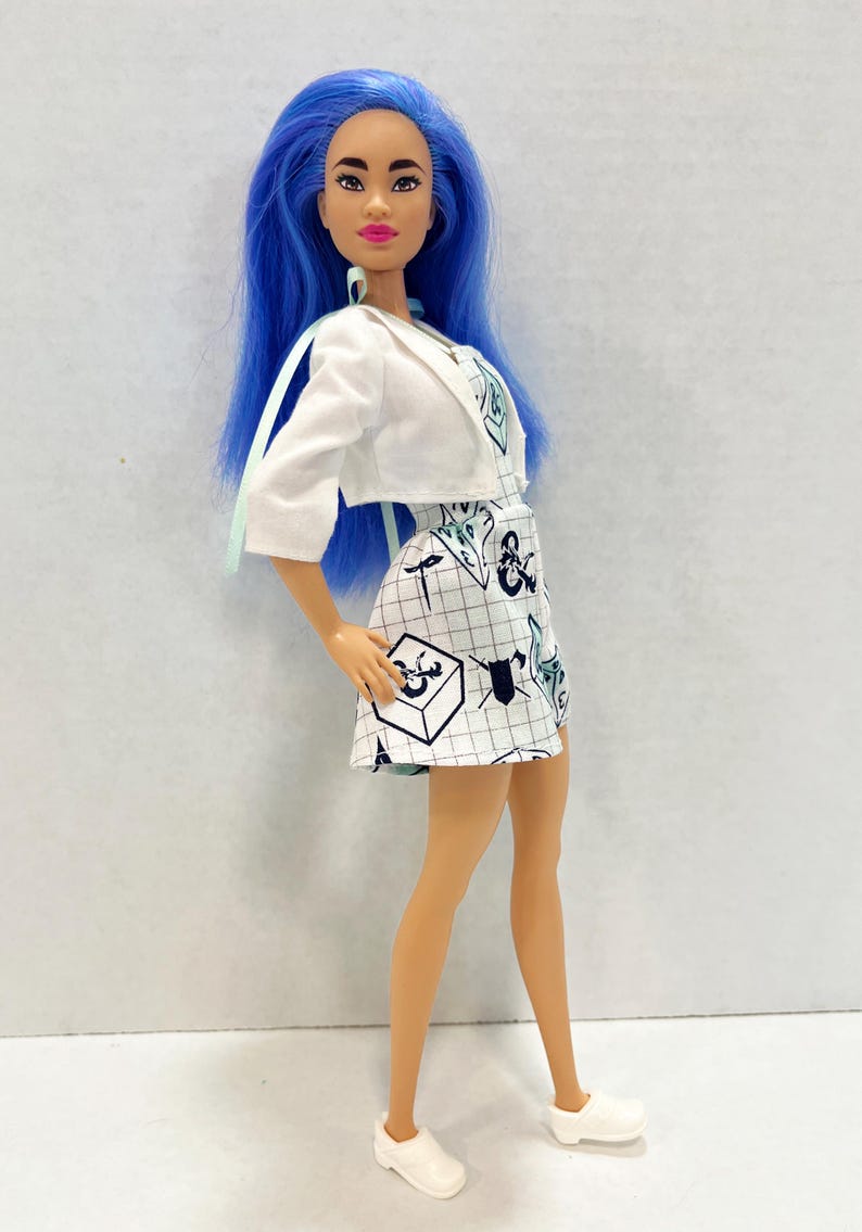 May include: A doll with long blue hair wearing a white cropped jacket over a white dress featuring a black grid pattern and various black and blue graphic symbols including shields and cubes. The doll wears simple white slip-on shoes on its feet.
